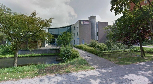 Vooraanzicht van het Cultuurhuis aan de Van Bleyswijckstraat met omliggende bomen en waterpartij.